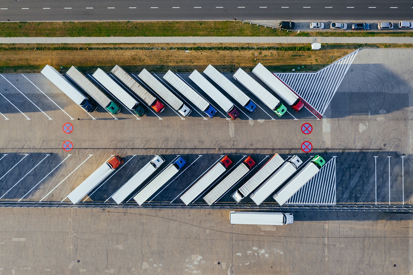 Das Bild zeigt einen Lkw-Parkplatz mit parallel geparkten Lastwagen. Die Fahrzeuge haben verschiedene Farben, und die Parkfläche liegt neben einer Straße.